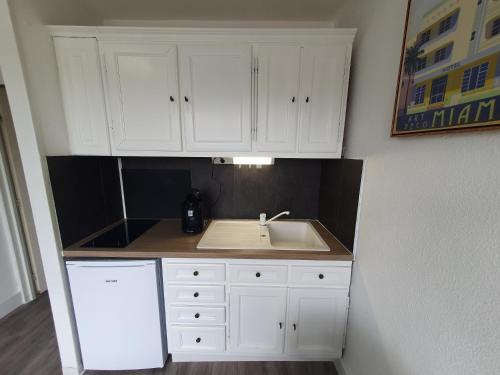 - une cuisine avec un évier et des placards blancs dans l'établissement Le studio mer, piscine et soleil, à La Grande Motte