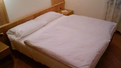 a bed with white sheets on it in a room at Campiglio Bilocale Dolomiti in Madonna di Campiglio