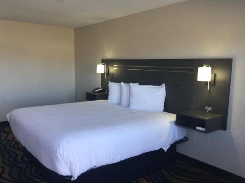 Habitación de hotel con cama grande con sábanas y almohadas blancas. en Americas Best Value Inn Muskogee, en Muskogee