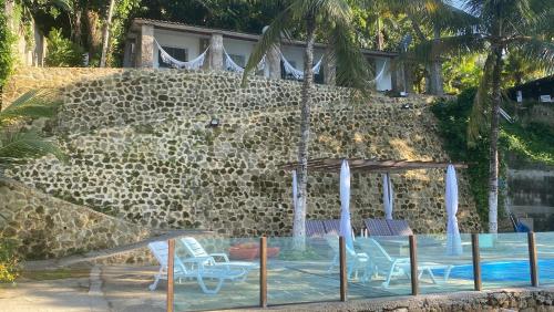 a swimming pool with chairs and a stone wall at Vivalavida Serra&Mar in Angra dos Reis
