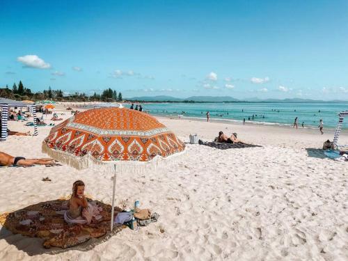 a woman sitting under an orange umbrella on a beach at Cosy Home Byron Bay in Byron Bay