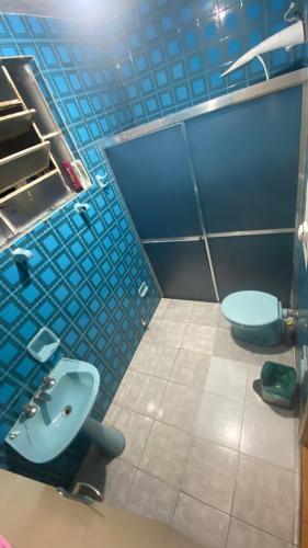 a blue tiled bathroom with a sink and a toilet at Quarto Aconchegante in Cruzeiro