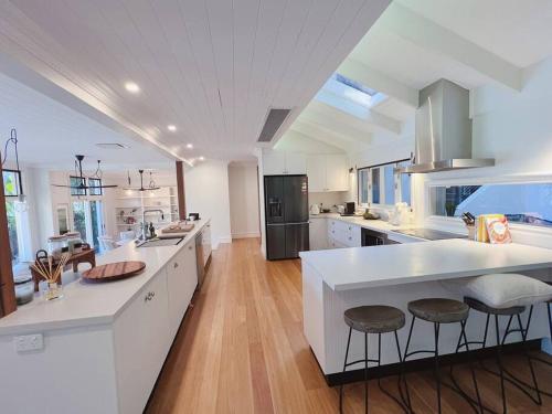una gran cocina con encimeras blancas y taburetes en Sydney’s Northern Beaches Waterfront Paradise, en Clareville