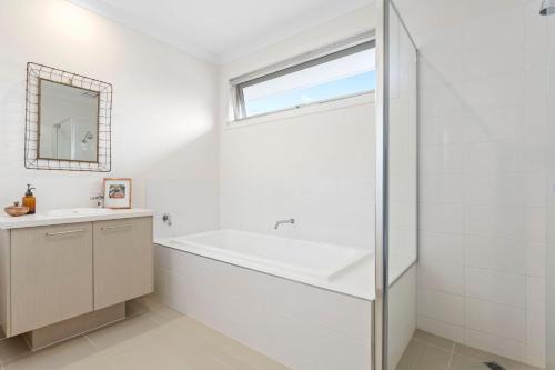 Un baño con bañera, lavabo y ventana. en Corymbia Mount Martha, en Mount Martha