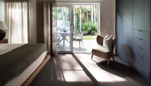 a bedroom with a bed and a chair and a sliding glass door at Tallowwood House Luxury Bed & Breakfast in Port Macquarie