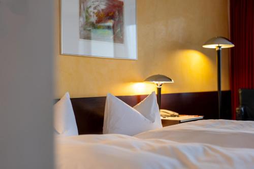 a bedroom with two beds with white sheets and lamps at Hotel Roth am Strande in Westerland