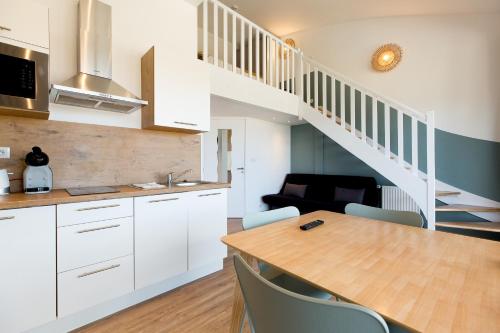 a kitchen with white cabinets and a wooden table at Appart'Hôtel Les Lofts du Grand Lac de Lozère in Langogne