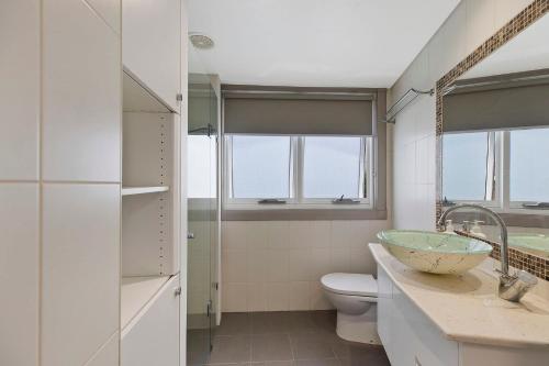a bathroom with a sink and a toilet and windows at Sandy Cove Apartment The Entrance 35 in The Entrance
