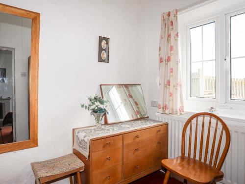 a room with a dresser with a mirror and a chair at Ty Hir in Llangoed