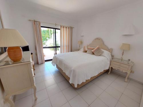 a white bedroom with a bed and a window at Ancão Beach Apartment in Almancil