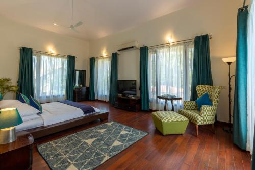 a bedroom with a bed and a chair and a television at ama Stays & Trails 25 Farm House, Vedic Village, Kolkata in Kolkata