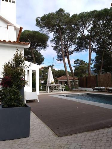 a swimming pool next to a house with a table and a umbrella at Banzão home PineForest family &friends pool garden in Colares