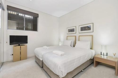 a white bedroom with a large bed and a flat screen tv at Luxury Apartments at Bells Blvd in Kingscliff