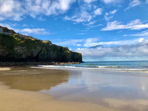 a sandy beach with the ocean and a cliff at WildView - Private Glamping For two with outdoor bath tub in Helston