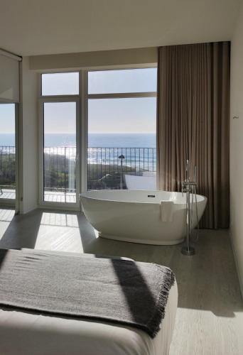 a large bathroom with a tub and a large window at Porto Covo Praia Hotel & SPA in Porto Covo