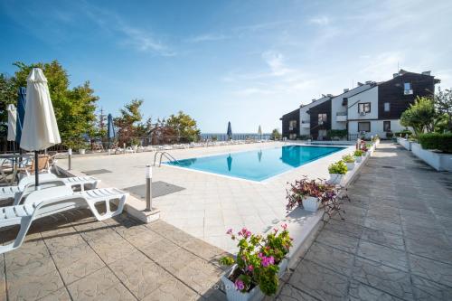 einen Pool mit Stühlen, einem Sonnenschirm und Blumen in der Unterkunft Apolon Complex in Sozopol