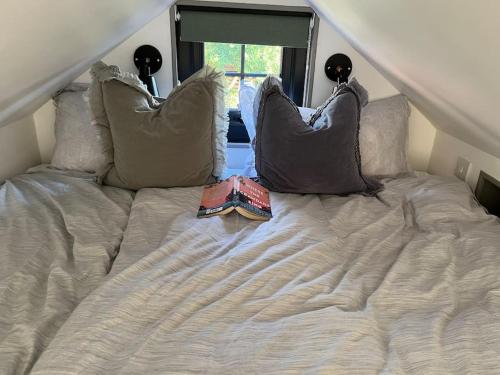 een bed met kussens en een boek erop bij Tiny guesthouse with cozy mezzanine sleeping nook in Swinderby