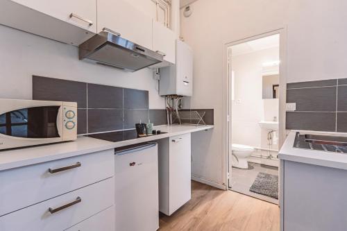 une cuisine avec des armoires blanches et un micro-ondes dans l'établissement Le Jardinet, face à la Cathédrale, baignoire - RDC, à Reims