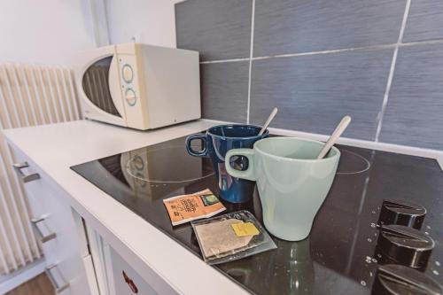 - un comptoir de cuisine avec 2 tasses et un four micro-ondes dans l'établissement Le Jardinet, face à la Cathédrale, baignoire - RDC, à Reims
