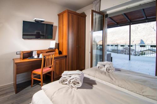 Cette chambre comprend deux lits, un bureau et une fenêtre. dans l'établissement Hotel Saligari, à Verceia