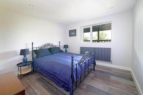 a bedroom with a blue bed and a window at Grove Lodge, Contemporary Cabin in Mendip Hills in Axbridge