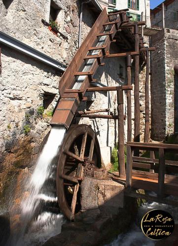 a watermill with a wooden wheel next to a building at B&B La Rosa Celtica in Capo di Ponte