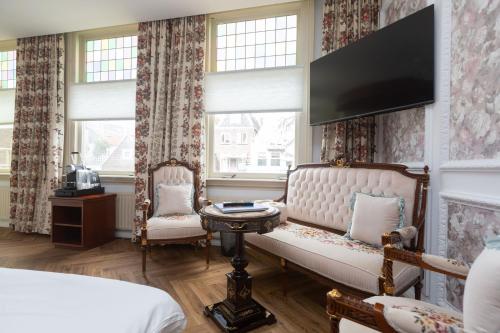 a bedroom with a couch and a tv on the wall at Hotel Johannes Vermeer Delft in Delft