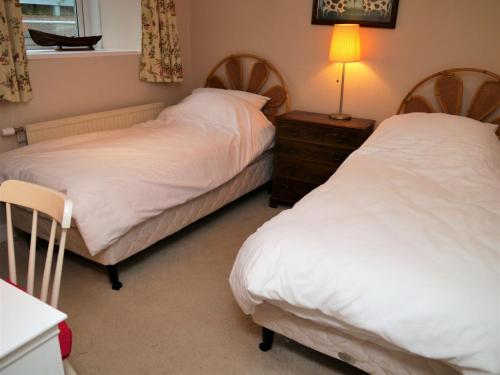 a bedroom with two beds and a table with a lamp at Phoenix Cottage in Kippford
