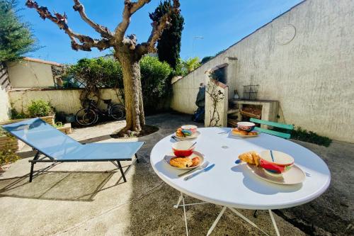 Biały stół z talerzami jedzenia i niebieskim krzesłem w obiekcie La Maison des Sauges - Village house with garden 500m from the beach w mieście Le Grau-du-Roi