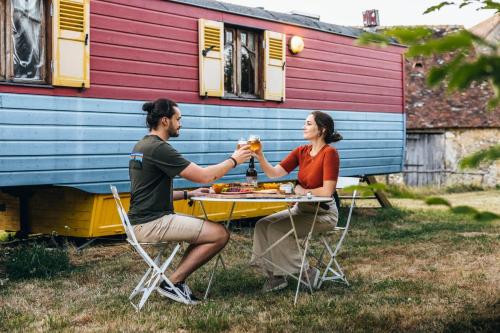 a man and woman sitting at a table in front of a house at Manoir du Bois Joly - Roulotte Art Déco in Margon