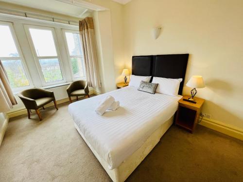 a bedroom with a bed and two chairs and windows at Heath Cottage Hotel in Dewsbury