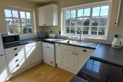 a kitchen with white cabinets and a sink and windows at Garden House in Cirencester