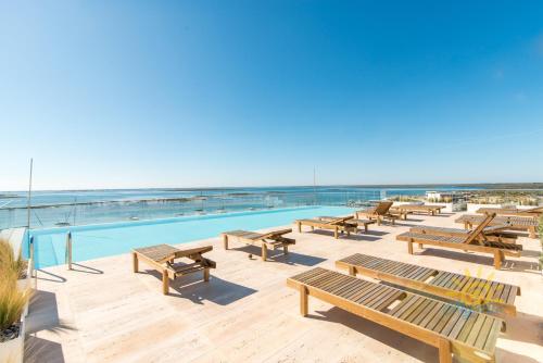 a pool with wooden benches next to the ocean at Luxo à Beira-Mar na Ria Formosa in Olhão