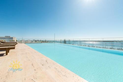 a large swimming pool with a view of the ocean at Luxo à Beira-Mar na Ria Formosa in Olhão