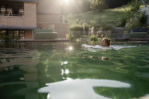 a woman is swimming in a swimming pool at HUBERTUS Mountain Refugio Allgäu in Balderschwang