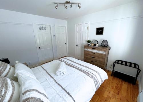 a white bedroom with a bed and a wooden dresser at Auberge musicale Pour un Instant in La Malbaie