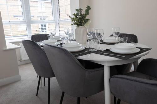 7 Swiftsure - 4 Bedroom Luxury and Spacious Home في ميلتون كينز: طاولة طعام مع كراسي وطاولة مع كؤوس للنبيذ