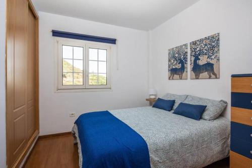 sypialnia z łóżkiem z niebieskimi prześcieradłami i oknem w obiekcie Apartamento en el casco histórico de San Mateo w mieście Vega de San Mateo