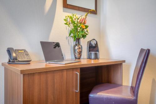 a desk with a laptop and a phone and a vase with flowers at Hotel Milano in Rotterdam