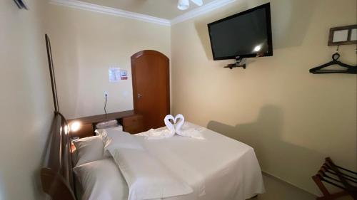 a room with a bed with white sheets and a tv at Espaço Nobre in Cunha
