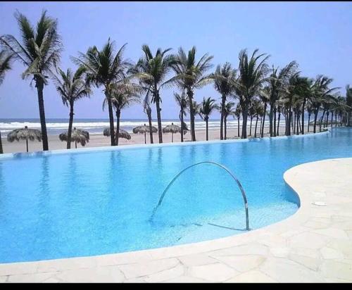 a swimming pool next to a beach with palm trees at Disfruta a lo grande en la Isla Residences Acapulco in Acapulco