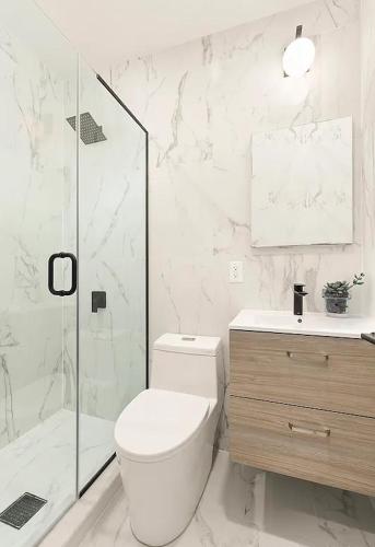 a white bathroom with a toilet and a shower at Designer Duplex near Central Park in New York