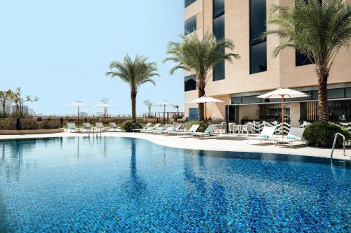 a swimming pool with chairs and palm trees in front of a building at Holiday Inn & Suites - Dubai Science Park, an IHG Hotel in Dubai