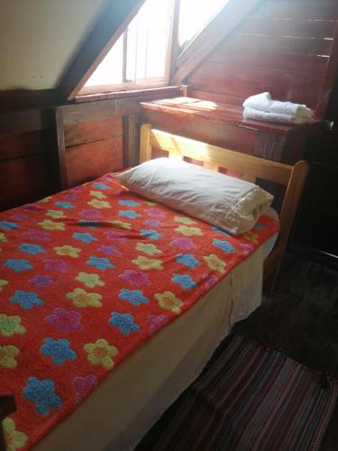 Una cama pequeña con una manta roja con flores. en Coffee Store La Cabaña en Valle Hornito