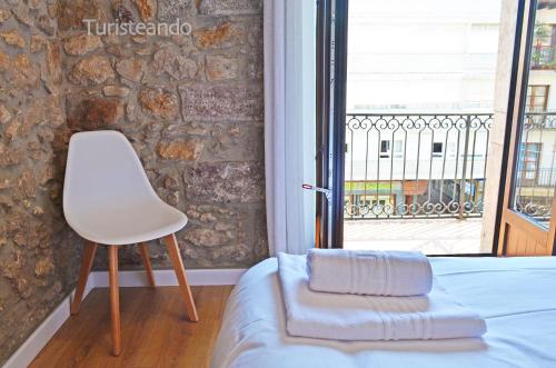 1 dormitorio con silla, cama y ventana en Apartamento Llerandi 2B - Totalmente reformado y con balcón al corazón de San Vicente de la Barquera, en San Vicente de la Barquera