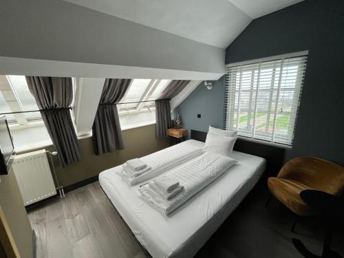 een slaapkamer met een bed, een stoel en ramen bij Hotel Oostereiland in Hoorn