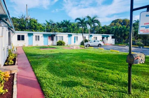 a green yard with a building and a parking lot at Hallandale Beach Motel in Hallandale Beach