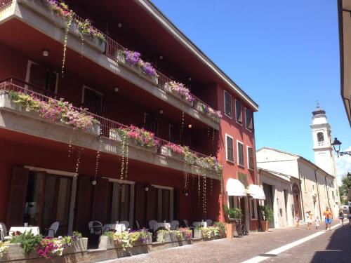 a red building with flowers on the balconies and a clock tower at Hotel Speranza in Bardolino