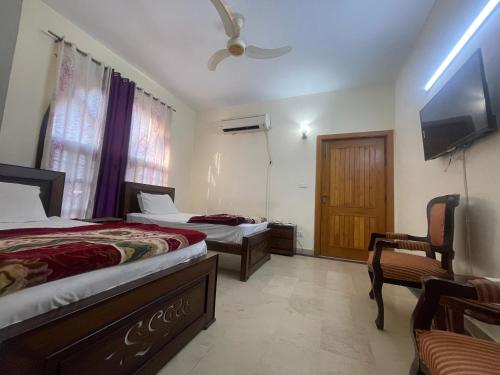 a bedroom with two beds and a tv and a chair at Dream Palace in Islamabad