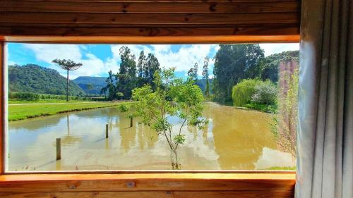 ein Fenster mit Blick auf einen überfluteten Fluss in der Unterkunft Pousada Mato Verde - Urubici - SC in Urubici